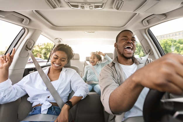 Joyeuse famille afro-américaine conduisant une nouvelle voiture en chantant en s'amusant