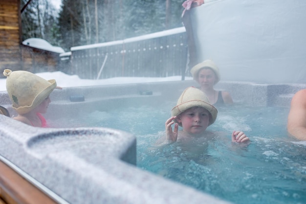 Joyeuse famille heureuse avec enfants profite d'un bain chaud dans un bain à remous jacuzzi par une froide journée d'hiver sans soucis