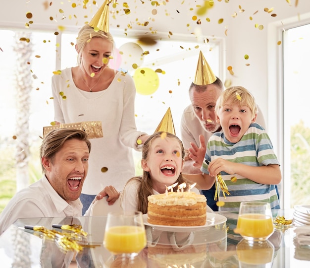 Joyeuse famille heureuse générationnelle portant des chapeaux de fête tout en célébrant l'anniversaire des petites filles avec des confettis et des gâteaux à la maison Enfants excités parents et grands-parents profitant d'un événement surprise spécial