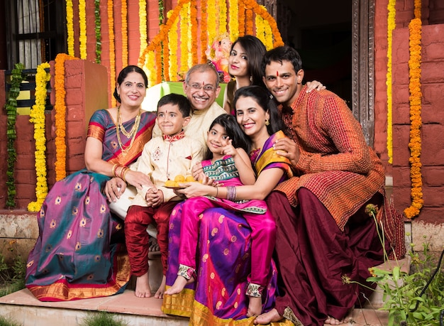 Joyeuse famille indienne célébrant le festival de Ganesh ou Chaturthi Accueillant ou jouant Pooja et mangeant des bonbons en tenue traditionnelle à la maison décorée de fleurs de souci