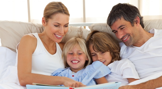 Joyeuse famille lisant un livre sur le lit