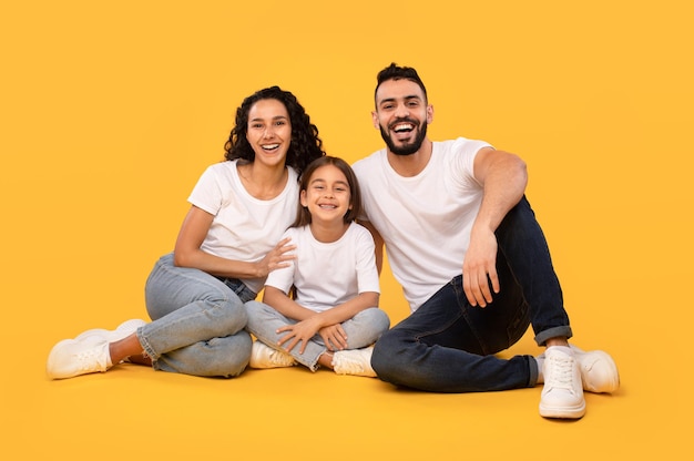 Joyeuse famille moyen-orientale de trois personnes assises sur fond jaune