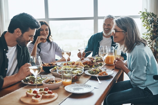 Joyeuse famille multigénérationnelle communiquant et souriant tout en dînant ensemble