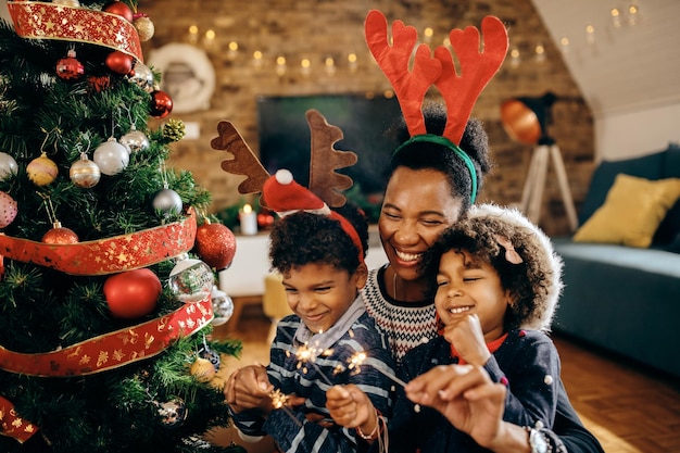 Joyeuse famille noire célébrant Noël et s'amusant avec des cierges magiques à la maison