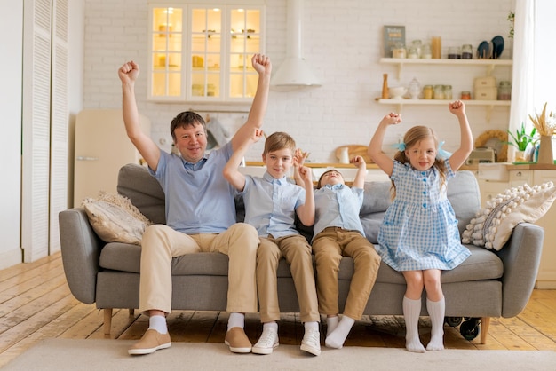 Joyeuse famille de pères ravis avec de petits enfants fans de sport regardant un match de télévision soutenant le thé de football...