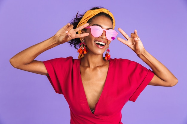 Joyeuse femme africaine en robe et lunettes de soleil montrant des gestes de paix