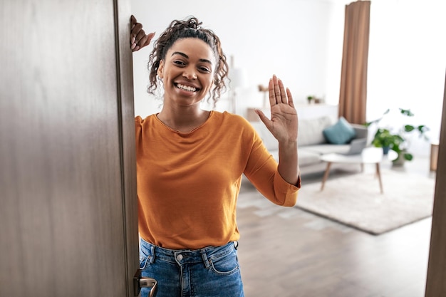Joyeuse femme afro-américaine agitant bonjour ouvrant la porte à la maison
