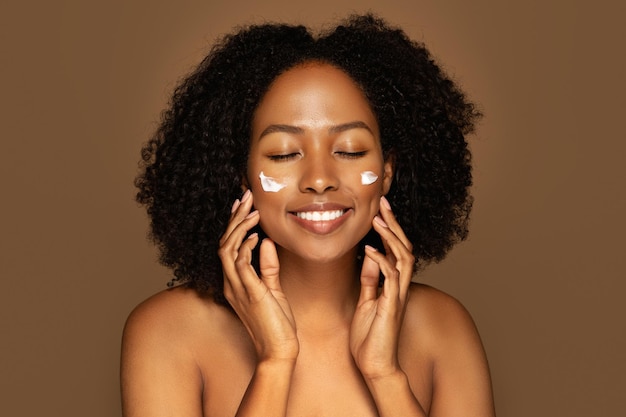 Joyeuse femme afro-américaine millénaire utilisant de la crème pour le visage