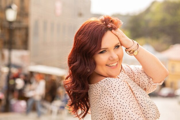 Joyeuse femme d'âge moyen aux cheveux rouges aux cheveux bouclés marchant dans la ville. Espace pour le texte