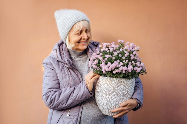 joyeuse femme âgée faisant un passe-temps et aime le jardinage. femme âgée portant des fleurs en pot