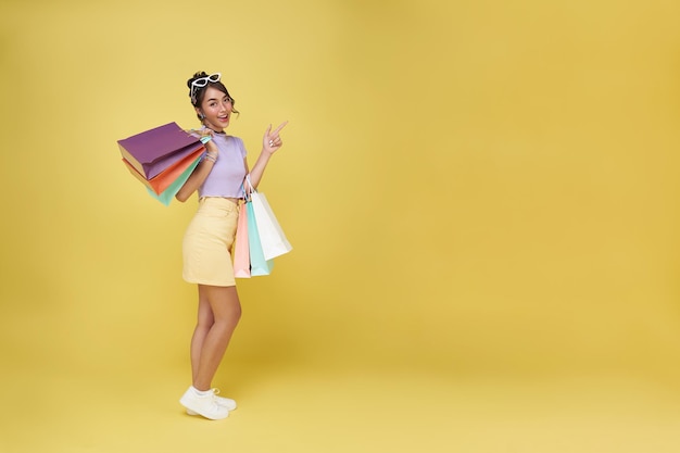 Joyeuse femme asiatique thaïlandaise heureuse appréciant le shopping elle porte des sacs à provisions doigt pointé