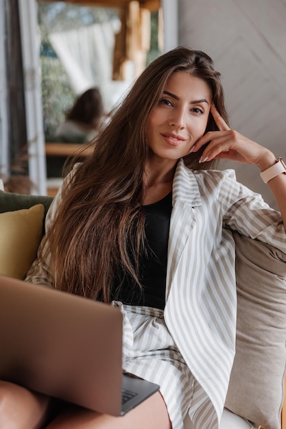 Joyeuse femme brune allongée sur un canapé et travaillant à distance dans un bungalow