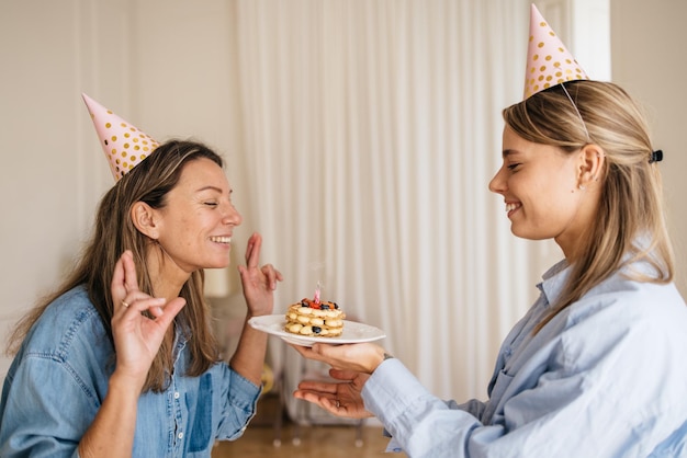 Joyeuse femme caucasienne adulte croise les doigts, fait un vœu en soufflant la bougie du gâteau tenu par un ami. Concept surprise