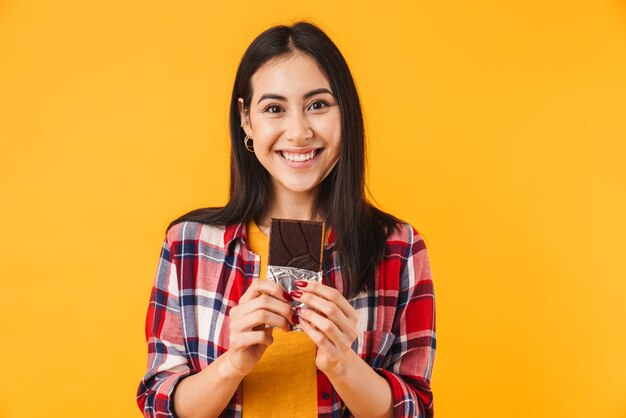 joyeuse femme caucasienne souriante et tenant du chocolat isolé sur un mur jaune