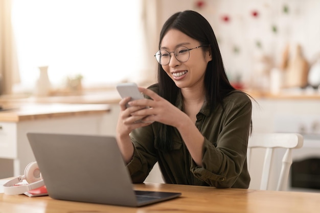 Joyeuse femme entrepreneure coréenne travaillant à domicile à l'aide de gadgets