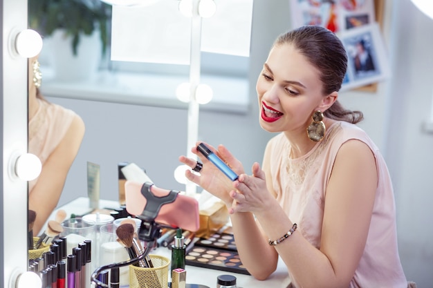 Joyeuse femme heureuse souriant tout en montrant son nouveau mascara à la caméra