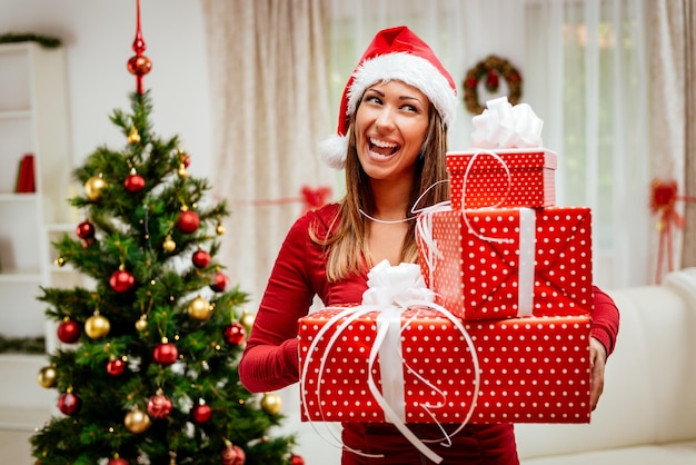 Joyeuse femme heureuse souriante avec un bonnet de noel sur la tête tenant des boîtes de cadeaux de noël pour surprendre quelqu'un.