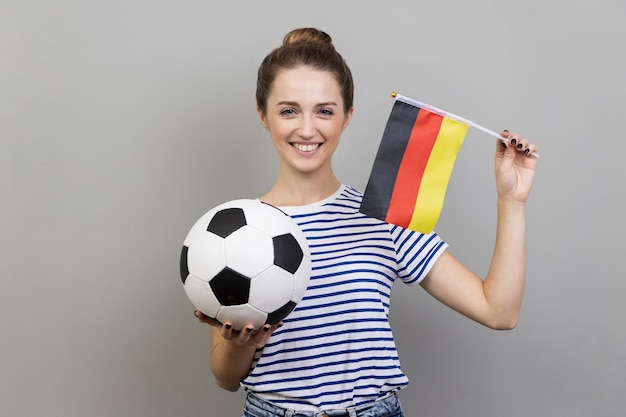 Joyeuse femme joyeuse tenant un ballon de football et un drapeau allemand regardant souriant à la caméra se réjouissant