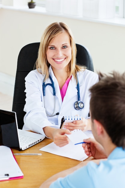 Joyeuse femme médecin donnant une prescription à son patient au bureau