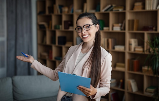 Joyeuse femme médecin européenne du millénaire invitant le client à faire un geste de la main à l'intérieur de la clinique de bureau