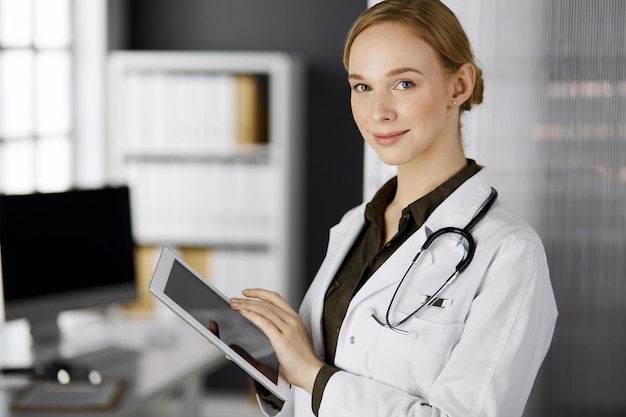 Joyeuse femme médecin souriante à l'aide d'un ordinateur tablette en clinique. Portrait d'une femme médecin sympathique au travail. Service médical parfait à l'hôpital. Notion de médecine.