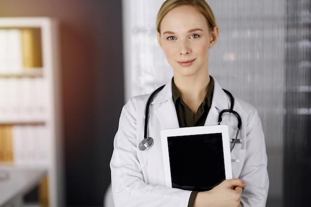 Joyeuse femme médecin souriante à l'aide d'un ordinateur tablette dans une clinique ensoleillée. Portrait d'une femme médecin sympathique au travail. Service médical parfait à l'hôpital. Notion de médecine.