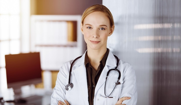 Joyeuse femme médecin souriante debout avec les bras croisés en clinique. Portrait d'une femme médecin sympathique. Notion de médecine.