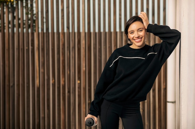 Joyeuse femme millénaire caucasienne en vêtements de sport avec une bouteille d'eau se reposant de l'exercice à l'extérieur