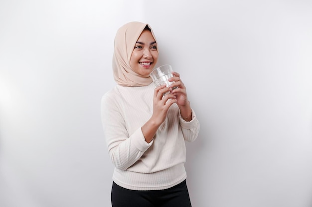 Joyeuse femme musulmane asiatique portant un foulard boit un verre d'eau isolé sur fond blanc