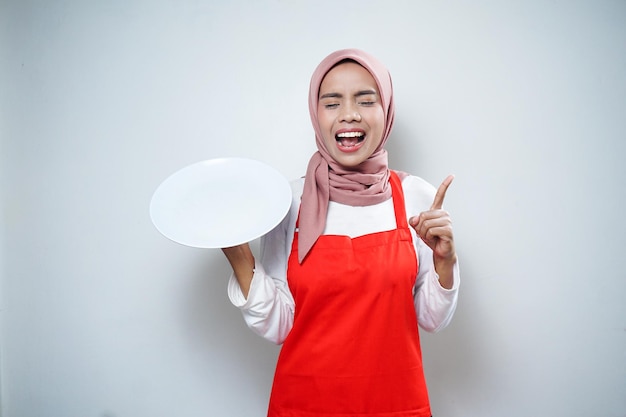 Joyeuse femme musulmane asiatique en tablier rouge tenant une assiette vide Publicité alimentaire Concept de cuisine