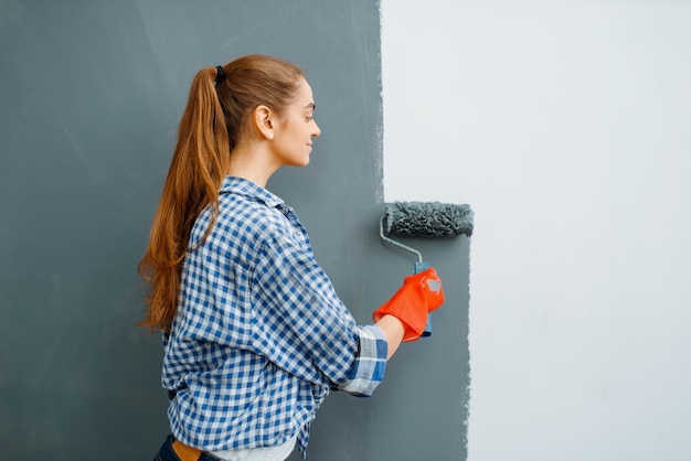 Joyeuse femme peintre en bâtiment peint les murs à l'intérieur.