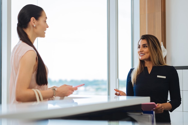 Joyeuse femme positive souriant au client en se tenant debout à la réception