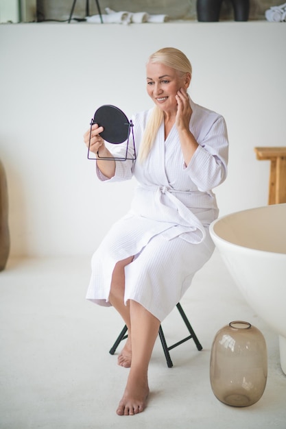 Joyeuse femme soignée examinant sa peau dans le miroir de poche