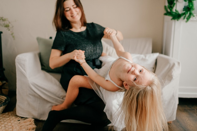 Joyeuse femme souriante tourbillonnant et jouant avec son adorable fille drôle dans une chambre confortable