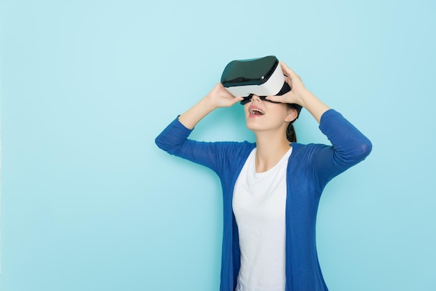 joyeuse femme tranquille debout sur fond bleu à l'aide d'un appareil de réalité virtuelle de produit technologique naviguant sur le site Web en ligne et visionnant une vidéo 3d se sentant surpris.