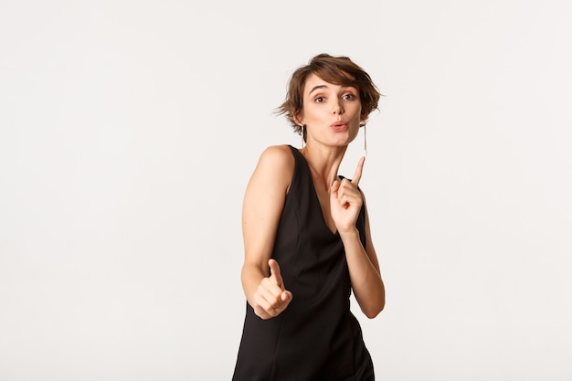 Joyeuse fêtarde s'amuser, danser en robe noire, debout sur blanc.