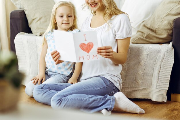 Joyeuse fête des mères! La petite fille félicite maman et lui donne une carte postale avec un dessin de coeur. Concepts de famille et d'enfance.
