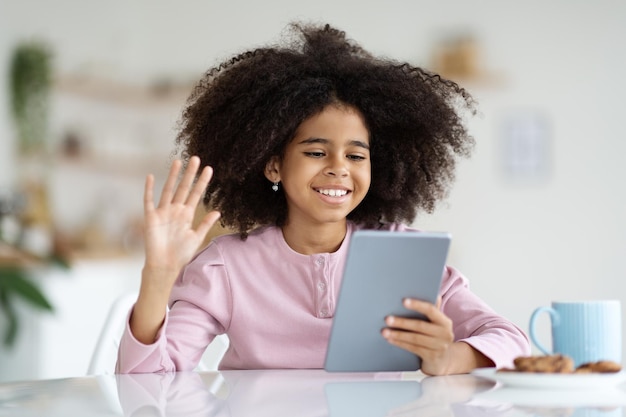 Joyeuse fille afro-américaine ayant un appel vidéo avec un ami