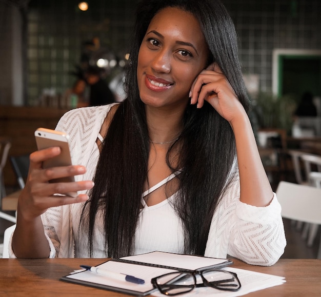 Joyeuse fille afro-américaine écrivant la liste des choses à faire et recevant un message sur un smartphone