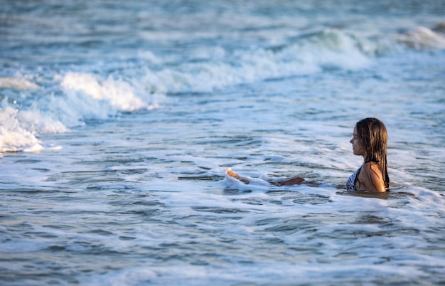 Joyeuse fille aux cheveux noirs et humides avec les cheveux mouillés dans un maillot de bain bikini léopard brillant éclabousse de l'eau autour d'elle et profite du soleil chaud tout en étant assise dans la mer bleue d'été