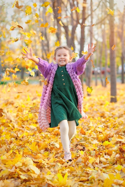 Photo joyeuse fille caucasienne riante de 5 ans s'amusant dans le parc d'automne s'exécute sous la chute des feuilles et se réjouit en automne