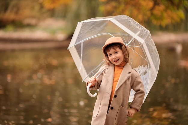 Joyeuse fille heureuse avec un parapluie transparent lors d'une promenade à l'automne au bord du lac