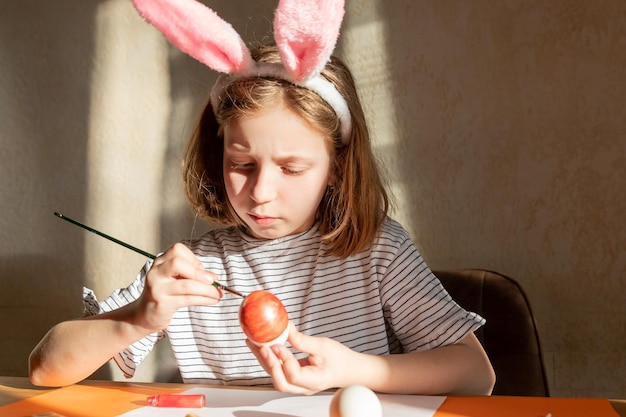 Joyeuse fille heureuse s'amusant et s'amusant tout en décorant des oeufs de pâques pour les vacances de printemps s'asseoir