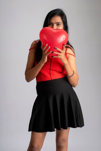 Joyeuse fille mignonne en costume rouge et noir fantaisie posant avec ballon en forme de coeur.
