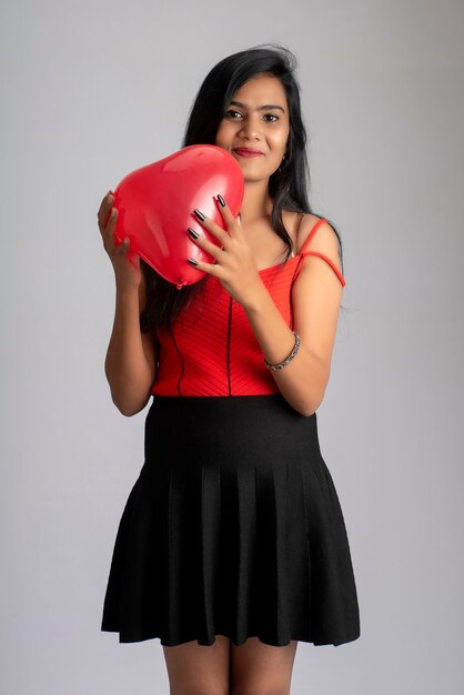 Joyeuse fille mignonne en costume rouge et noir fantaisie posant avec ballon en forme de coeur.