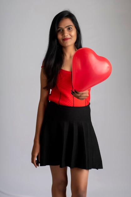 Joyeuse fille mignonne en costume rouge et noir fantaisie posant avec ballon en forme de coeur.