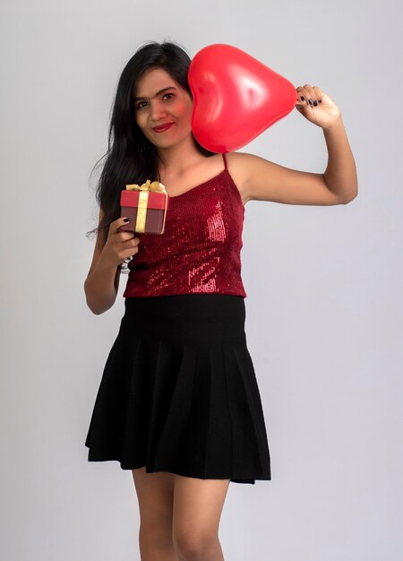 Joyeuse fille mignonne en tenue de fantaisie posant avec ballon en forme de coeur et boîte-cadeau.