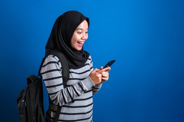 joyeuse fille musulmane asiatique en train de naviguer sur Internet ou de lire un message de discussion sur son téléphone