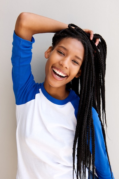 Joyeuse fille noire avec des cheveux tressés souriant contre un mur