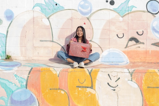 La joyeuse fille portant un chapeau de fête avec une boîte-cadeau assise sur un fond coloré